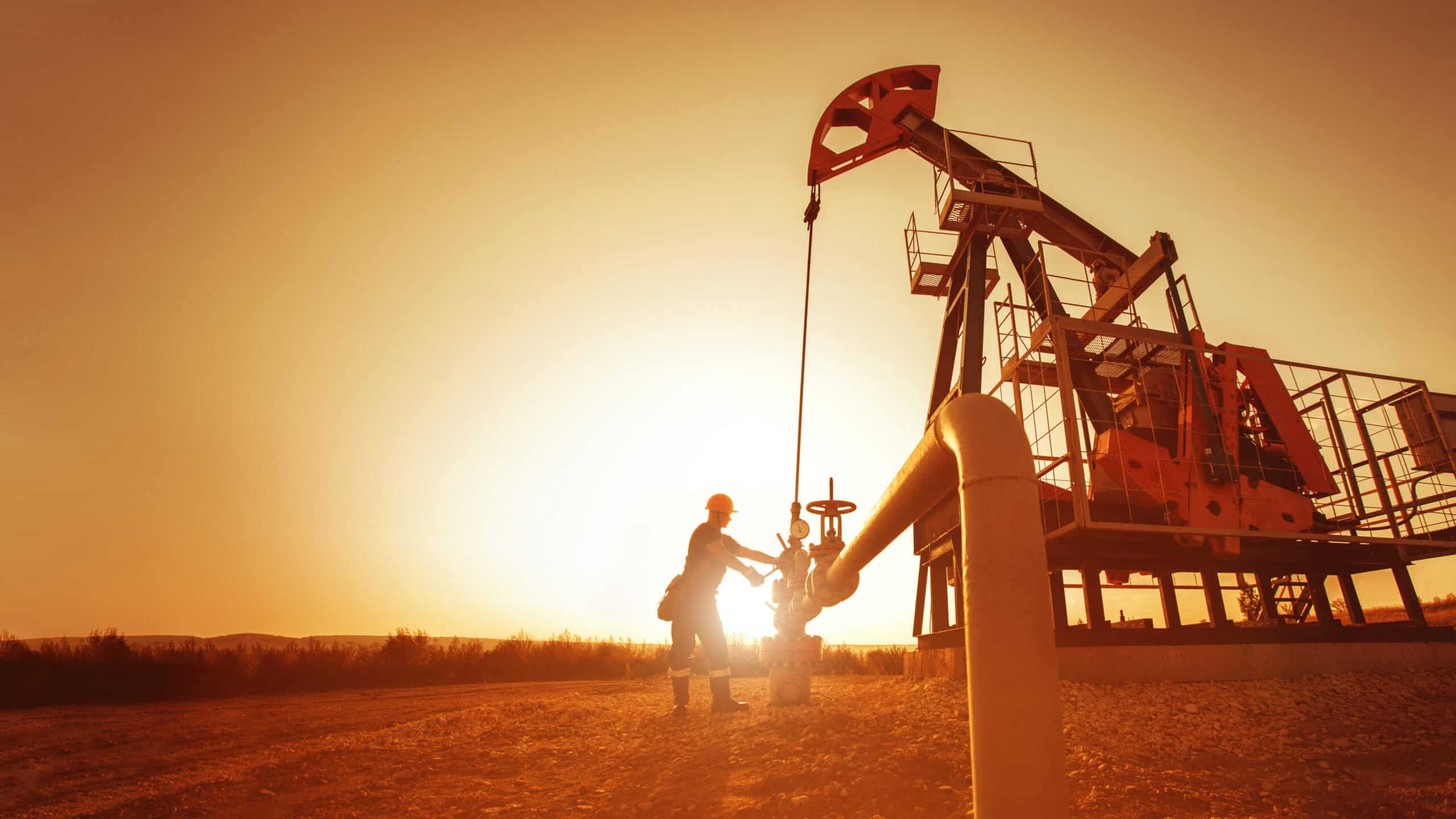 Oil worker is checking the pump near oil derrick on the sunset b